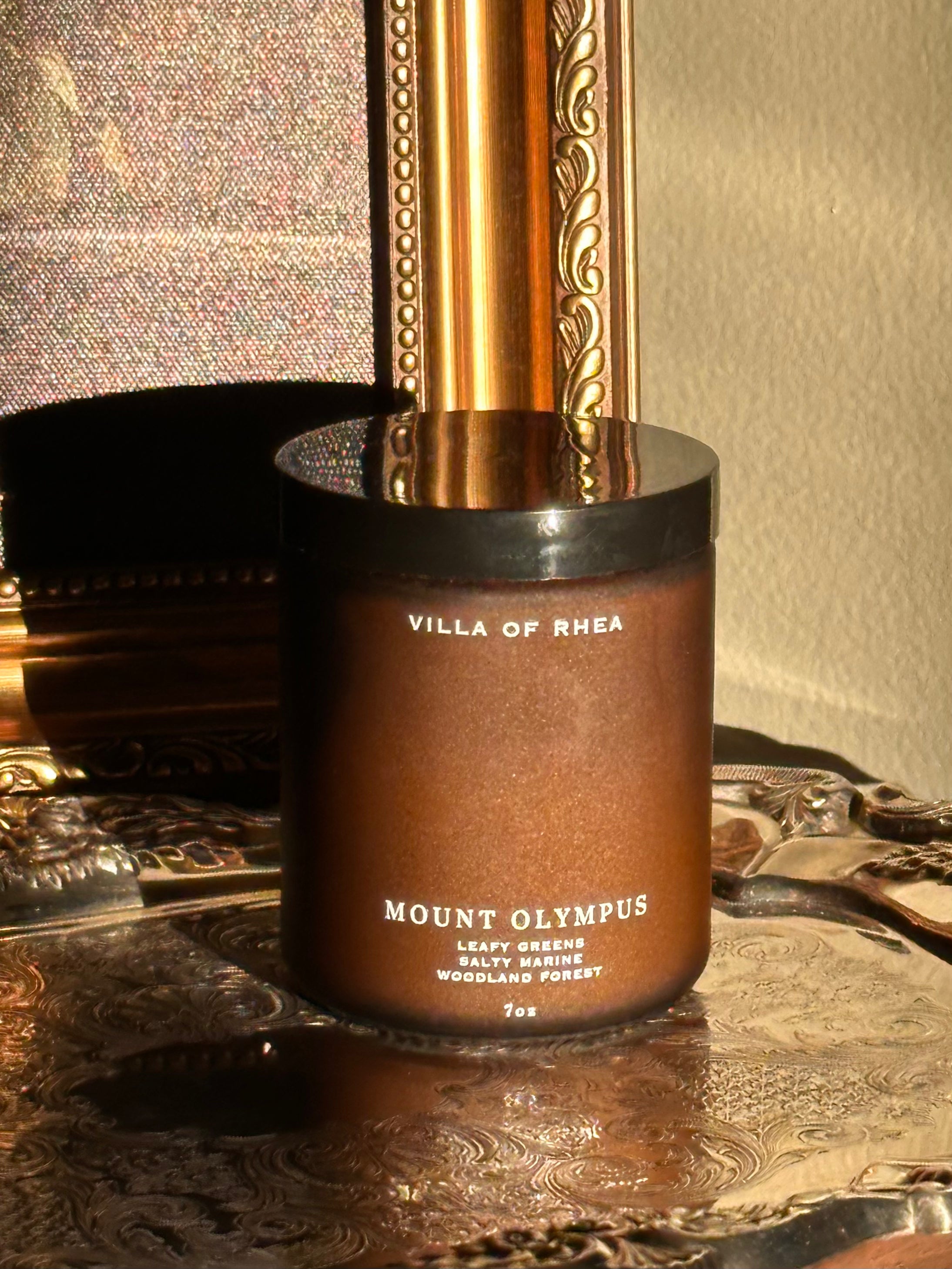 Mount Olympus candle on a decorative surface with a mirror in the background. leafy greens, salty marine, woodland forest scent . Vintage style. greek mythology inspired. luxurious soy wax candies.