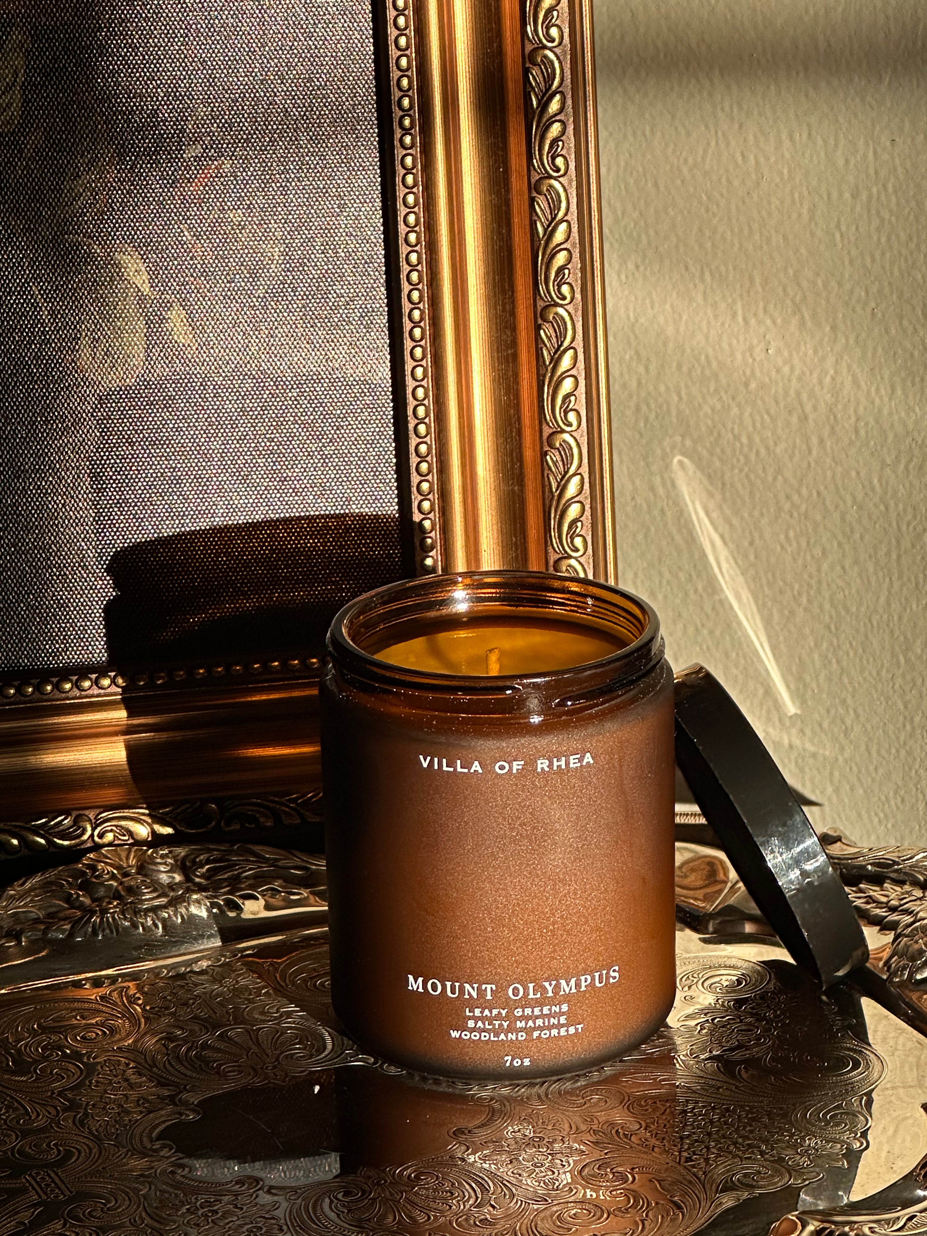 Mount Olympus candle on a decorative surface with a mirror in the background. leafy greens, salty marine, woodland forest scent . Vintage style. greek mythology inspired. luxurious soy wax candies.