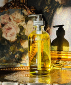 Collection of perfume bottles on a decorative tray with a classical painting in the background. Gaia fragrance free body oil.  on a decorative tray with floral elements and a classical statue in the background. Vintage style. Greek Mythology Inspired. Luxury Body Oils