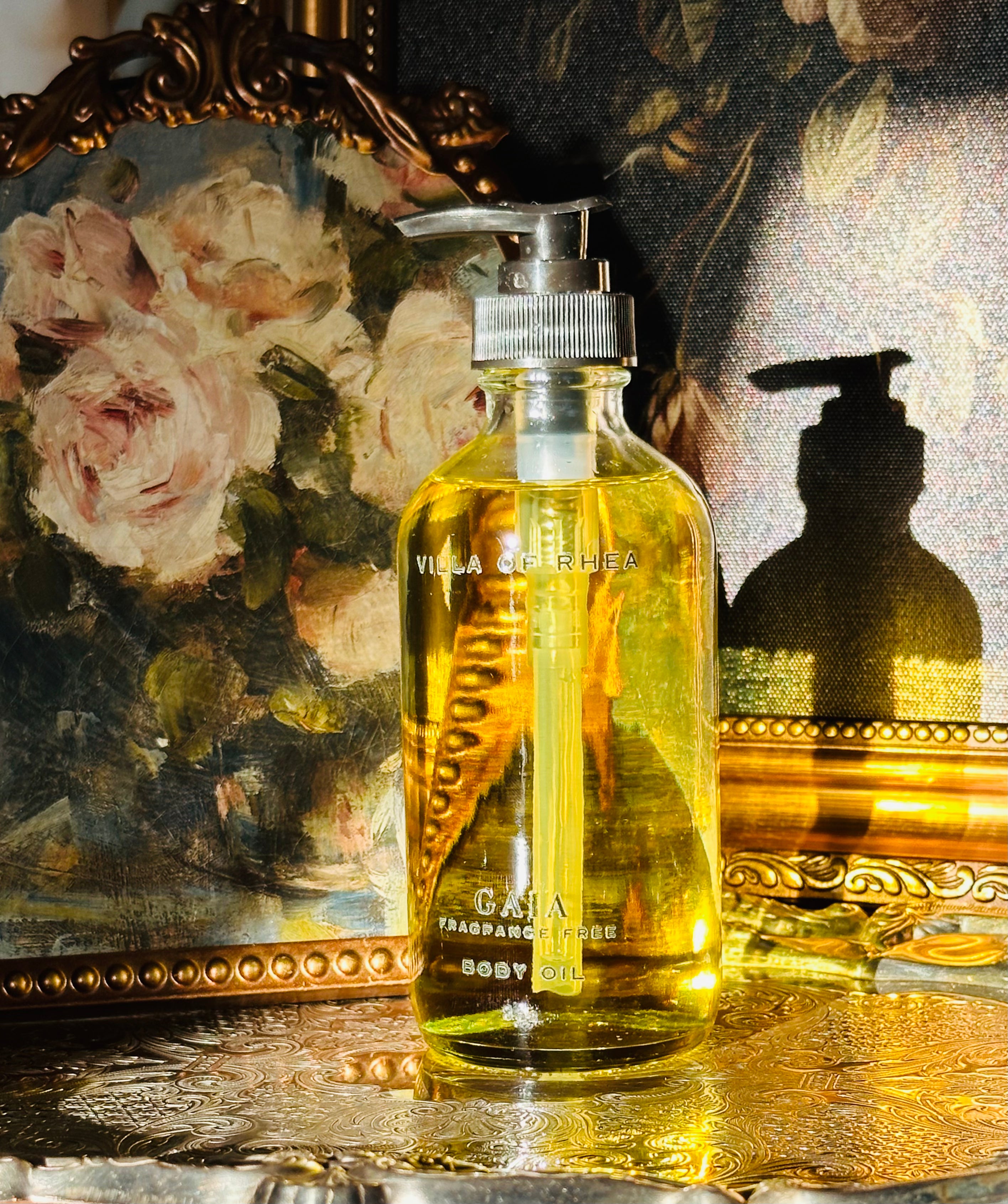 Collection of perfume bottles on a decorative tray with a classical painting in the background. Gaia fragrance free body oil.  on a decorative tray with floral elements and a classical statue in the background. Vintage style. Greek Mythology Inspired. Luxury Body Oils