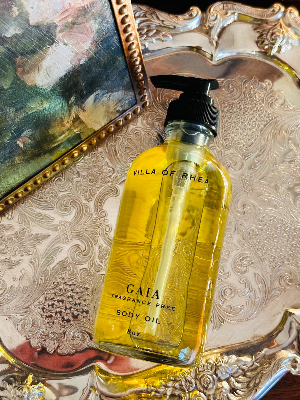 Collection of perfume bottles on a decorative tray with a classical painting in the background. Gaia fragrance free body oil.  on a decorative tray with floral elements and a classical statue in the background. Vintage style. Greek Mythology Inspired. Luxury Body Oils