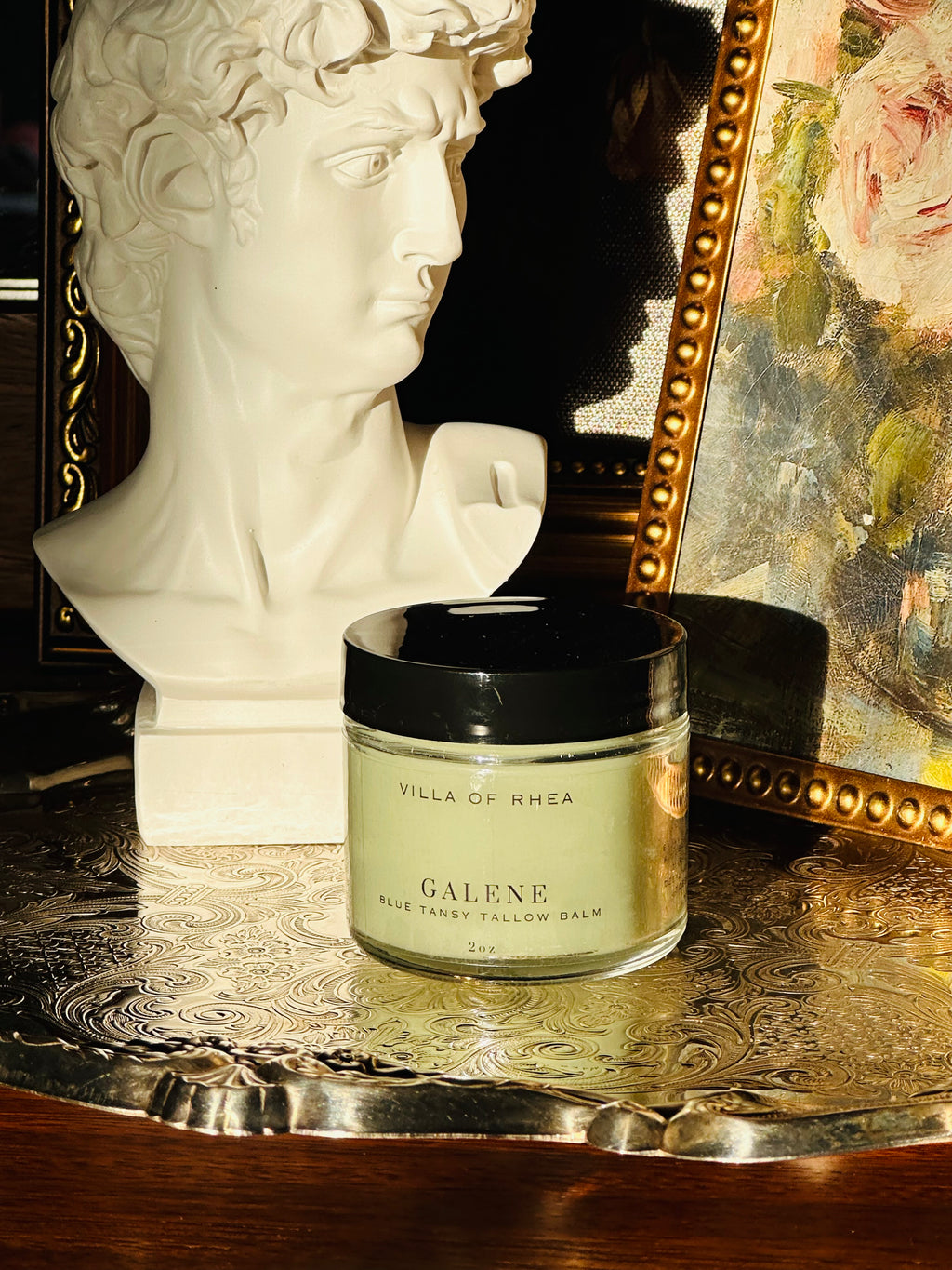 Jar of 'Galene Blue Tansy Tallow Balm' from 'Villa of Rhea' on a decorative surface with a mirror and statue in the background. Vintage style. Greek Mythology Inspired. Luxury tallow balm. luxurious handmade tallow balm.