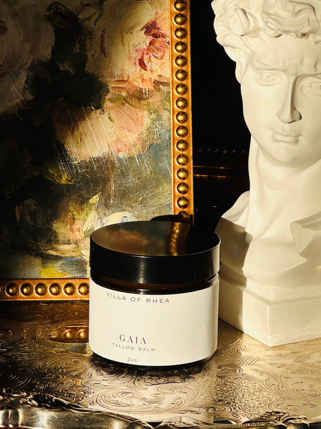 Jar of 'Gaia Tallow Balm' from 'Villa of Rhea' on a decorative surface with a mirror and statue in the background. Vintage style. Greek Mythology Inspired. Luxury tallow balm. luxurious handmade tallow balm.