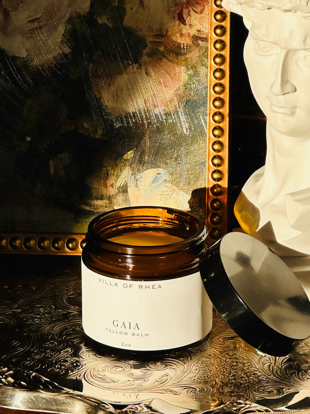 Jar of 'Gaia Tallow Balm' from 'Villa of Rhea' on a decorative surface with a mirror and statue in the background. Vintage style. Greek Mythology Inspired. Luxury tallow balm. luxurious handmade tallow balm.
