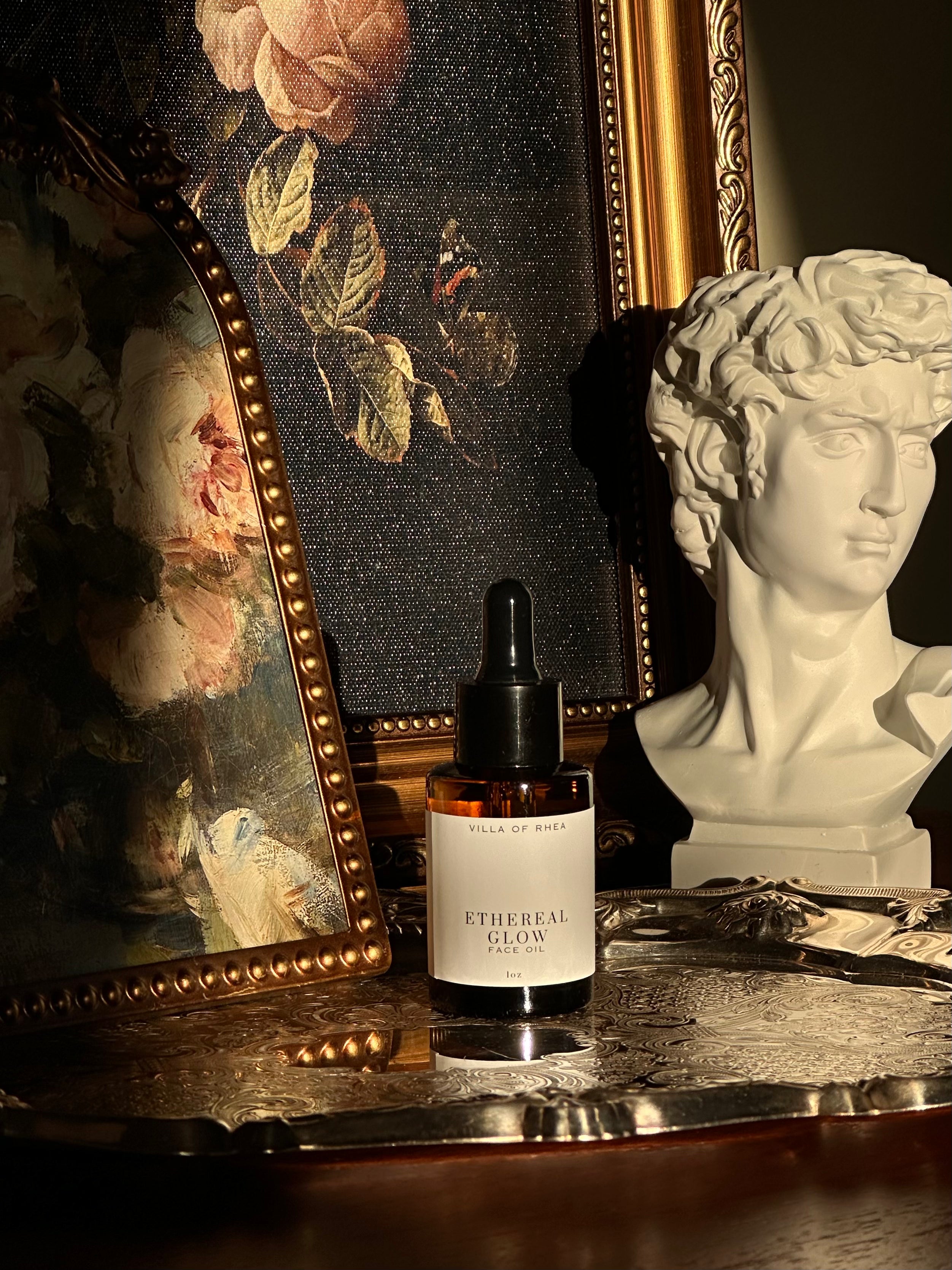 Bottle of 'Ethereal Glow' serum on a reflective surface with classical sculpture and painting in the background.Vintage style. Greek Mythology Inspired. Luxury Face Oils