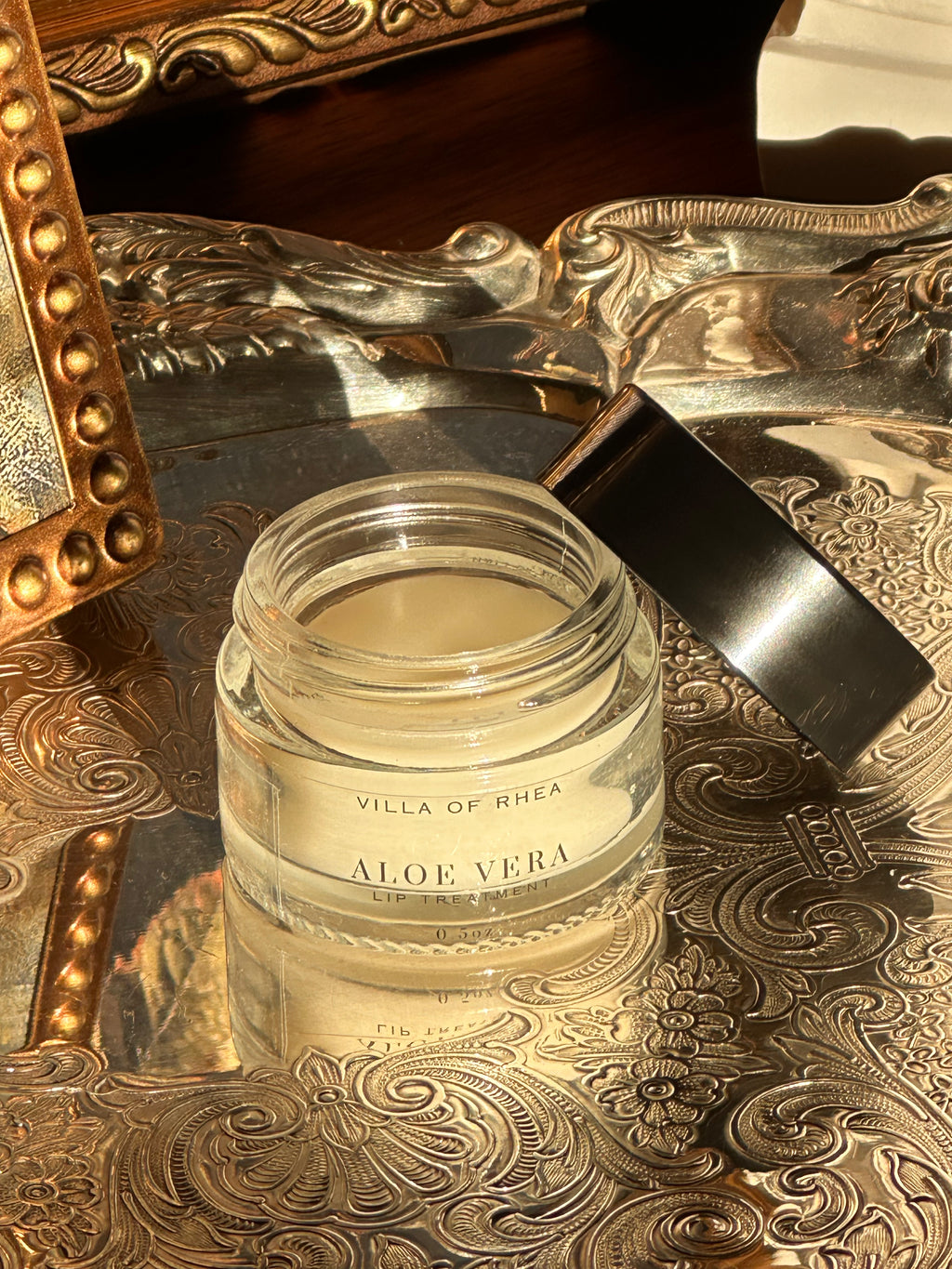 Jar of Villa of Rhea Aloe Vera lip balm on a decorative metal tray with a reflective background.Vintage style. Greek Mythology Inspired. Luxury lip balm. luxurious lip treatment