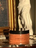 Sugar scrub named 'Aphrodite' on a reflective surface with classical sculpture in the background .Vintage style. Greek Mythology Inspired. Luxury body scrub. handmade body scrubs.