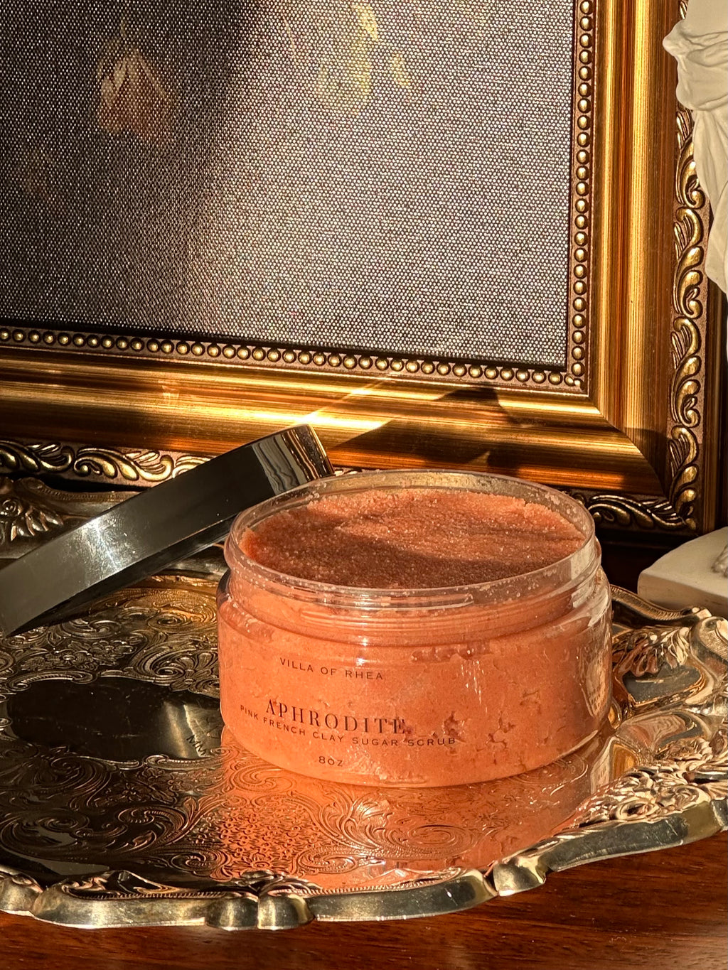 Sugar scrub named 'Aphrodite' on a reflective surface with classical sculpture in the background .Vintage style. Greek Mythology Inspired. Luxury body scrub. handmade body scrubs.