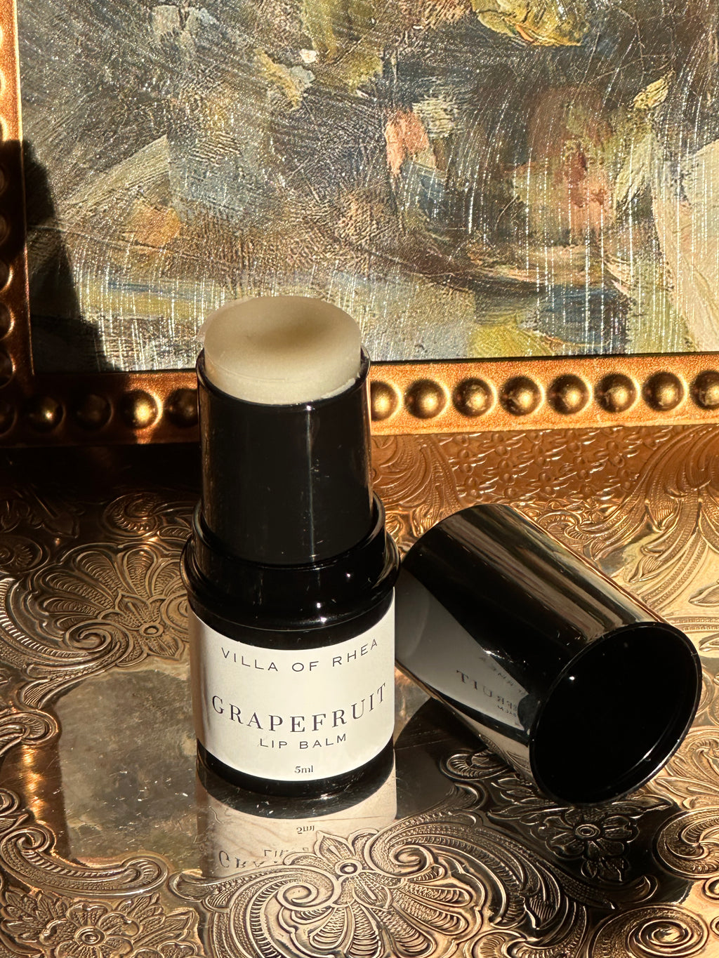Villa of Rhea Grapefruit Lip Balm on a decorative surface with a textured background.Vintage style. Greek Mythology Inspired. Luxury lip balm. luxurious handmade lip balm