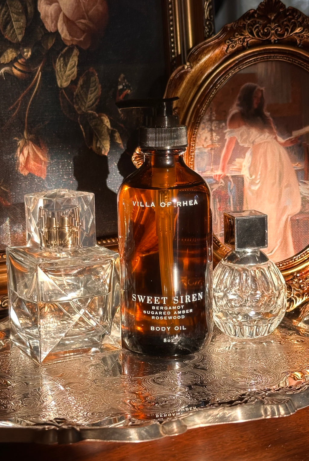 Villa of Rhea Sweet Siren body oil bottle on a reflective surface with decorative background.Sweet Siren Body Oil. Bergamot, Sandalwood, Amber, Pear scent. All Natural Skin Care. Non-Toxic Body Care, Greek Mythology Inspired. Chic Skincare. Chic Aesthetic. Minimalistic Aesthetic