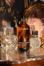 Villa of Rhea Sweet Siren body oil bottle on a reflective surface with decorative background.Sweet Siren Body Oil. Bergamot, Sandalwood, Amber, Pear scent. All Natural Skin Care. Non-Toxic Body Care, Greek Mythology Inspired. Chic Skincare. Chic Aesthetic. Minimalistic Aesthetic