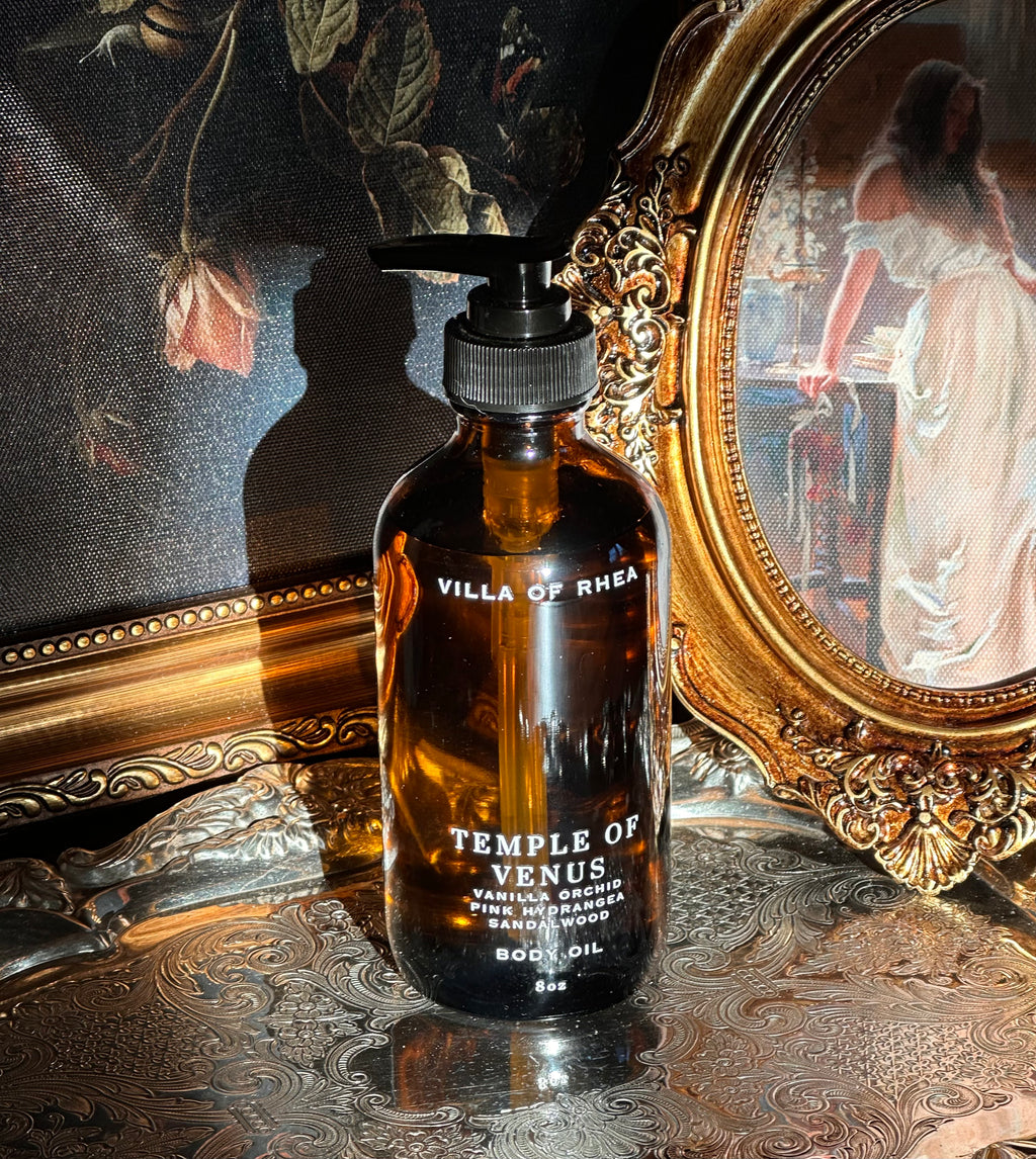 Villa of Rhea body oil bottle with classical statue and floral painting in the background.Temple of Venus Body Oil. Vanilla Scent. Orchid Scent. Hydrangea and Sandalwood Fragrance. Aphrodite Goddess. Greek Mythology inspired. Vintage Modern Style. All Natural body oil. Non-toxic Body Care. Healthy Clean Beauty. Green Beauty. Healthy Body Oil